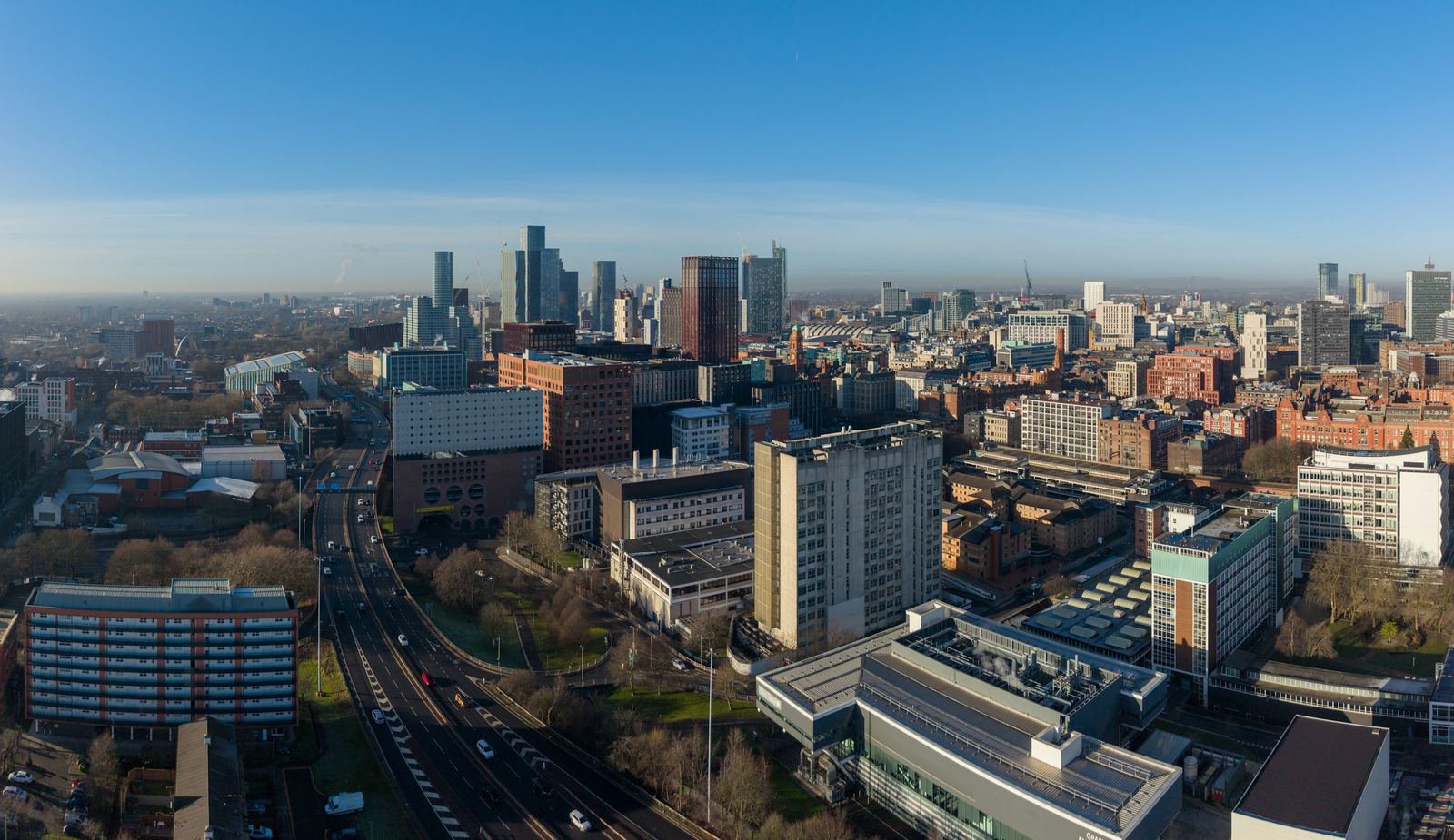 Manchester from above on a clear morning, the Mancunian Way curving past the city centre towers
