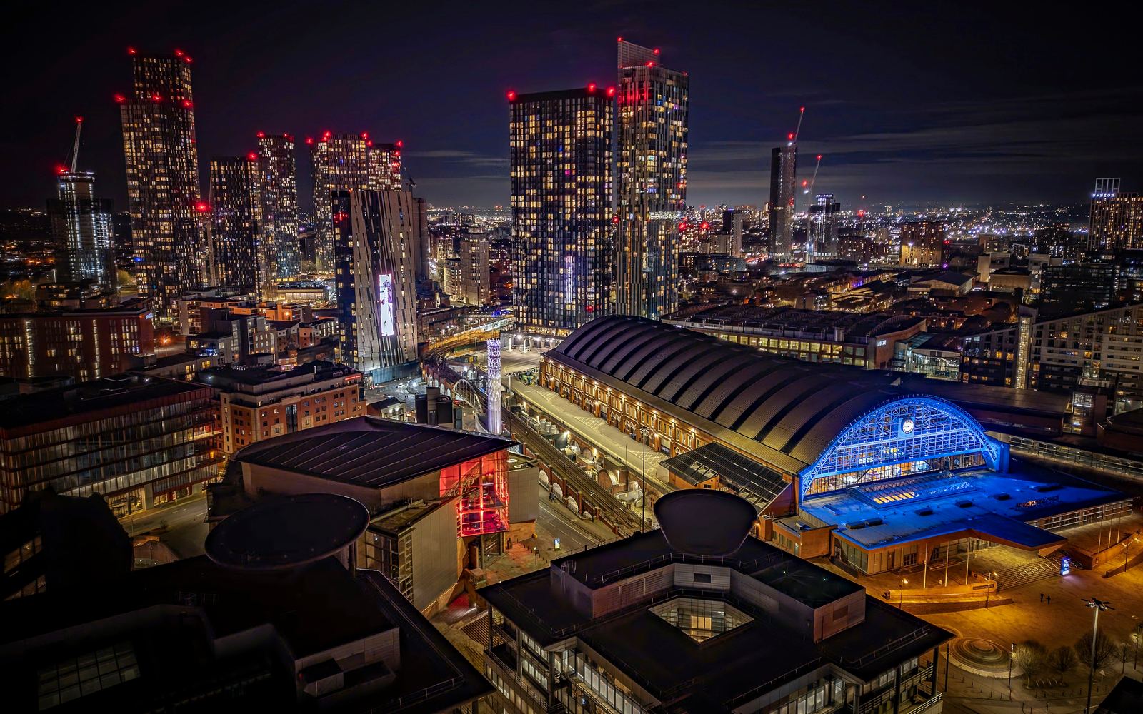 Manchester city centre at night, with tower cranes lit by red aviation lights above new apartment towers